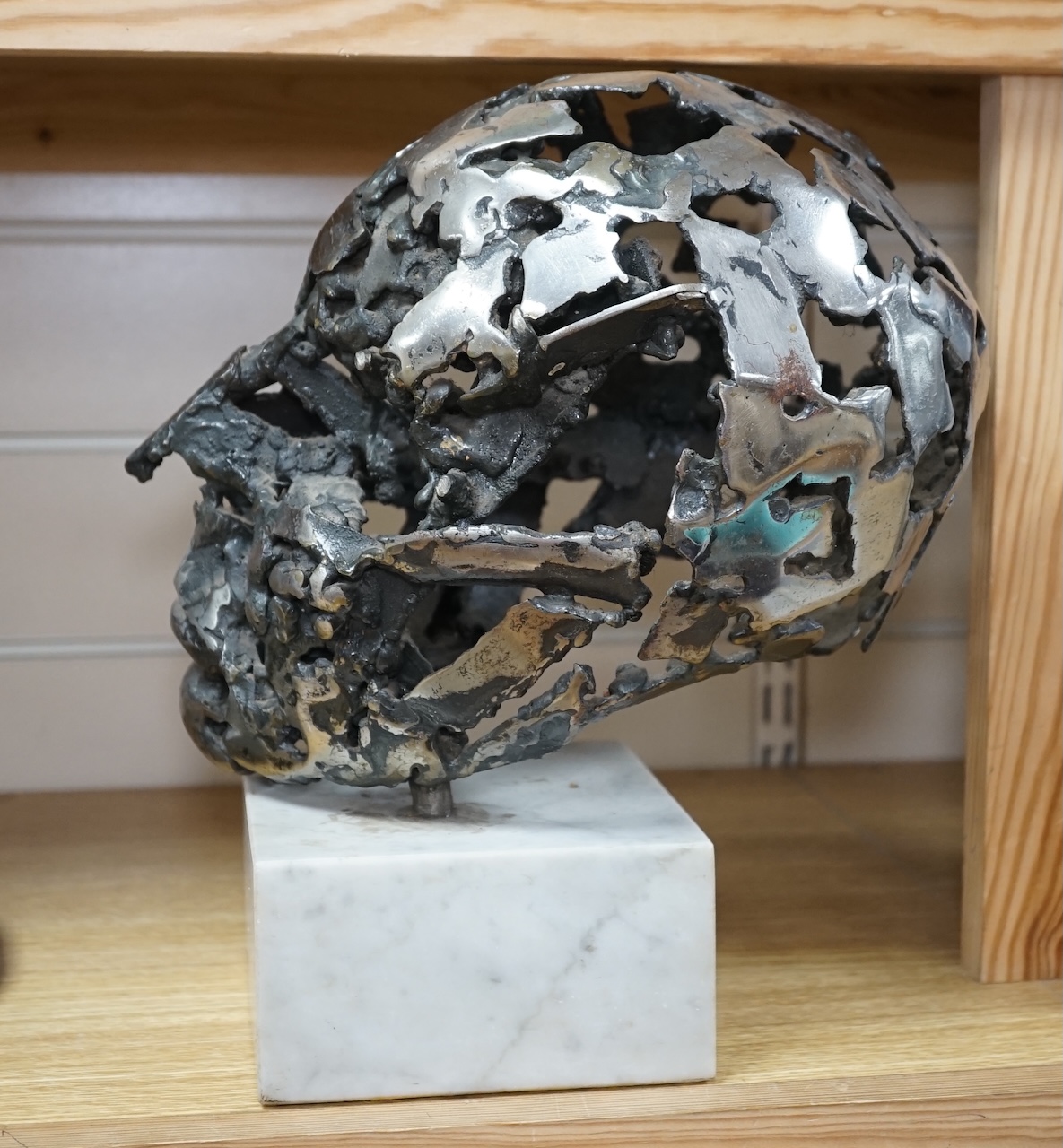 A modern polished steel skull, pierced and mounted on square white marble plinth, circa 1975, 31cm high. Condition - good, minor chipping